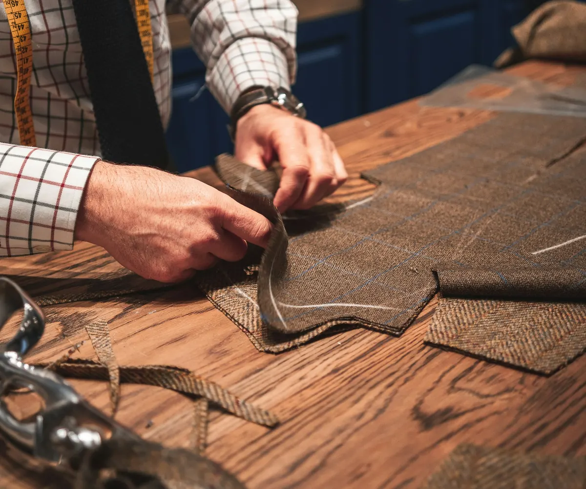 A tailor's hands shaping tweed on a wooden cutting table