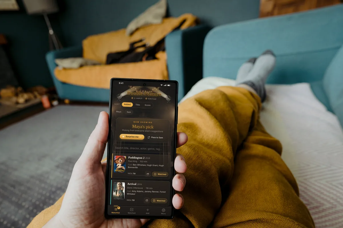 A phone open to the Double Feature watchlist, held by someone stretched out on a sofa