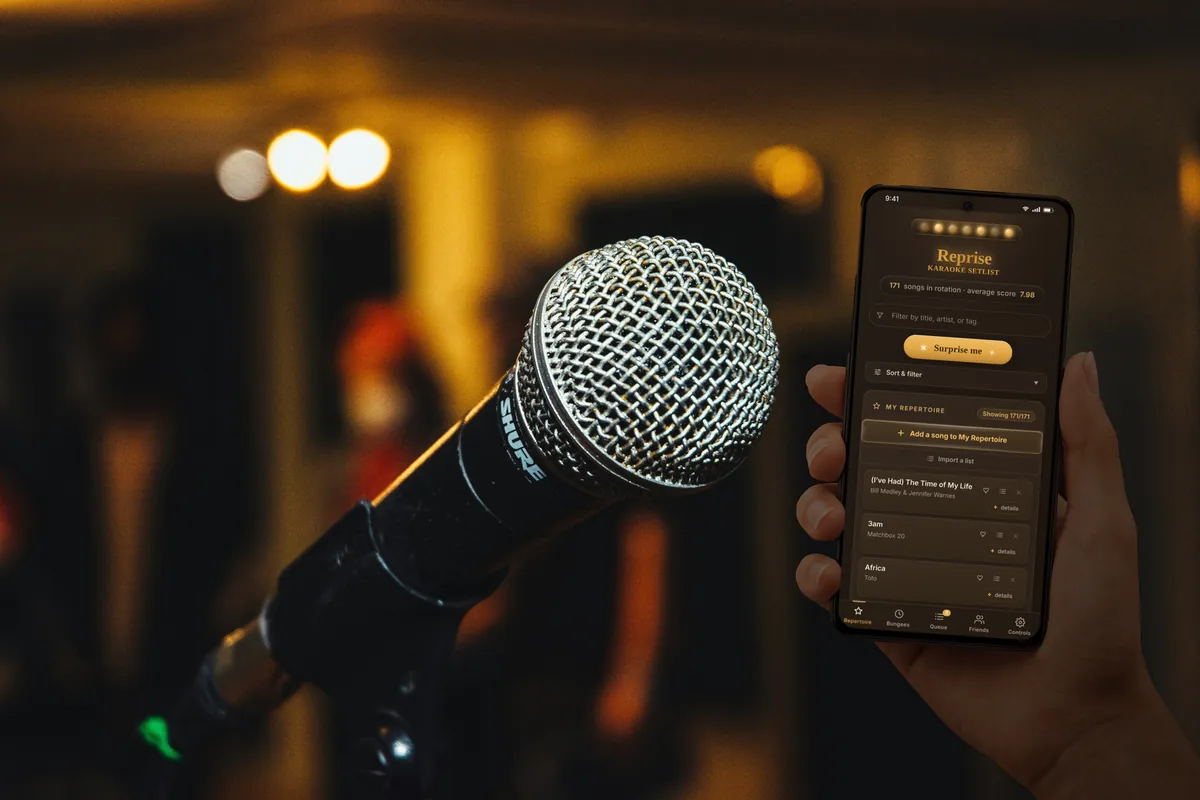 A hand holding a phone open to Reprise beside a microphone in a dim karaoke bar